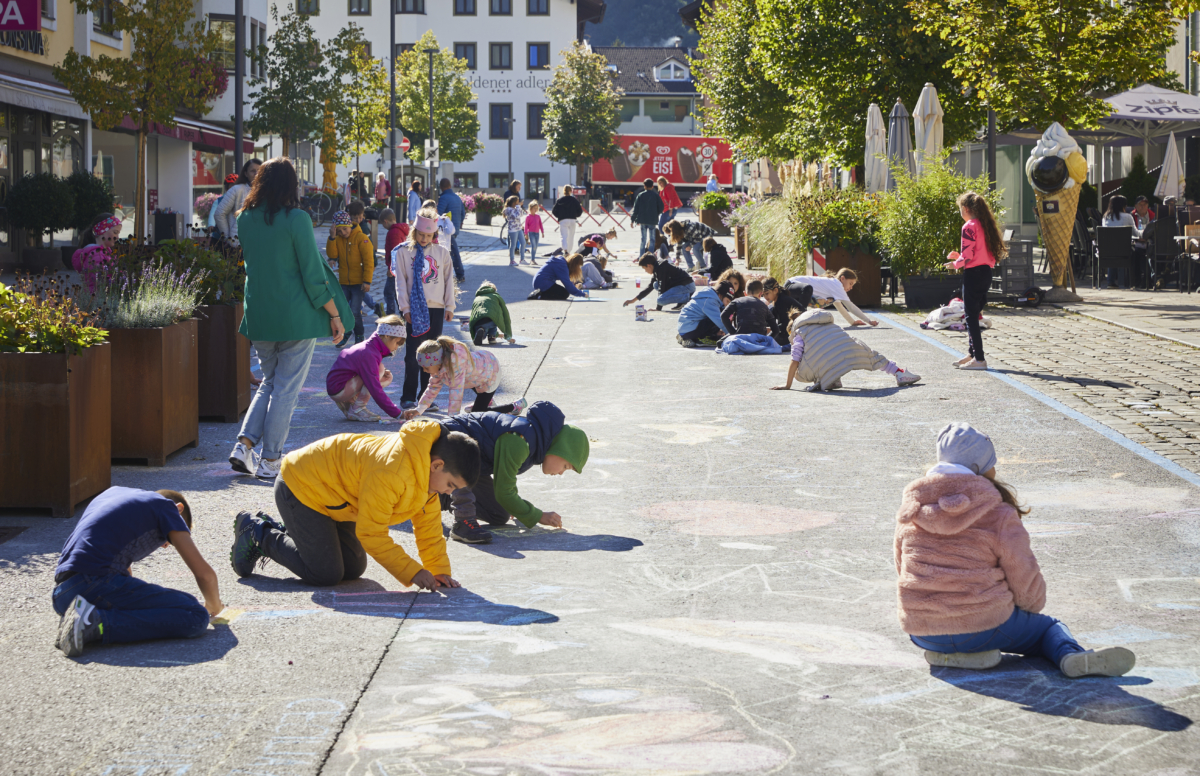 Kinder malen mit Kreide in der Klimabündnis gemeinde Wattens auf der Straße bei Sonnenschein
