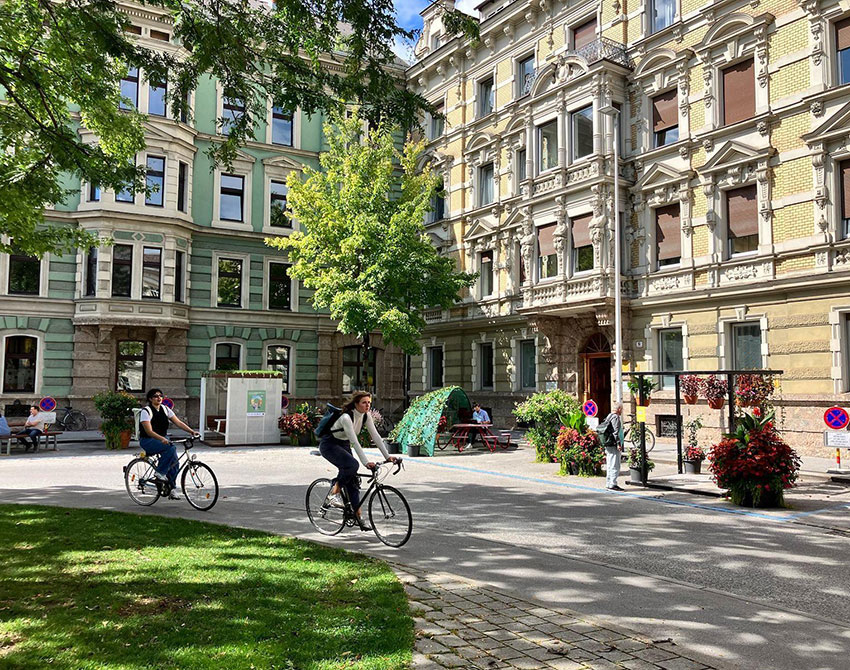 Zwei Radfahrende fahren am begrünten Adolf-Pichler-Platz in Innsbruck.