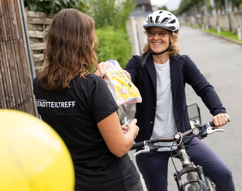 Eine Frau auf dem Fahrrad nimmt ein Frühstückssackerl entgegen.