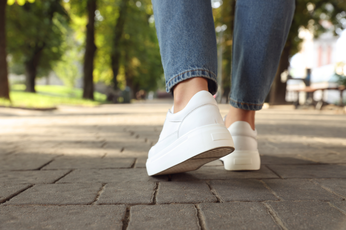 Person geht auf Pflaster. Zwei Füße in weißen Schuhen, Jeans.