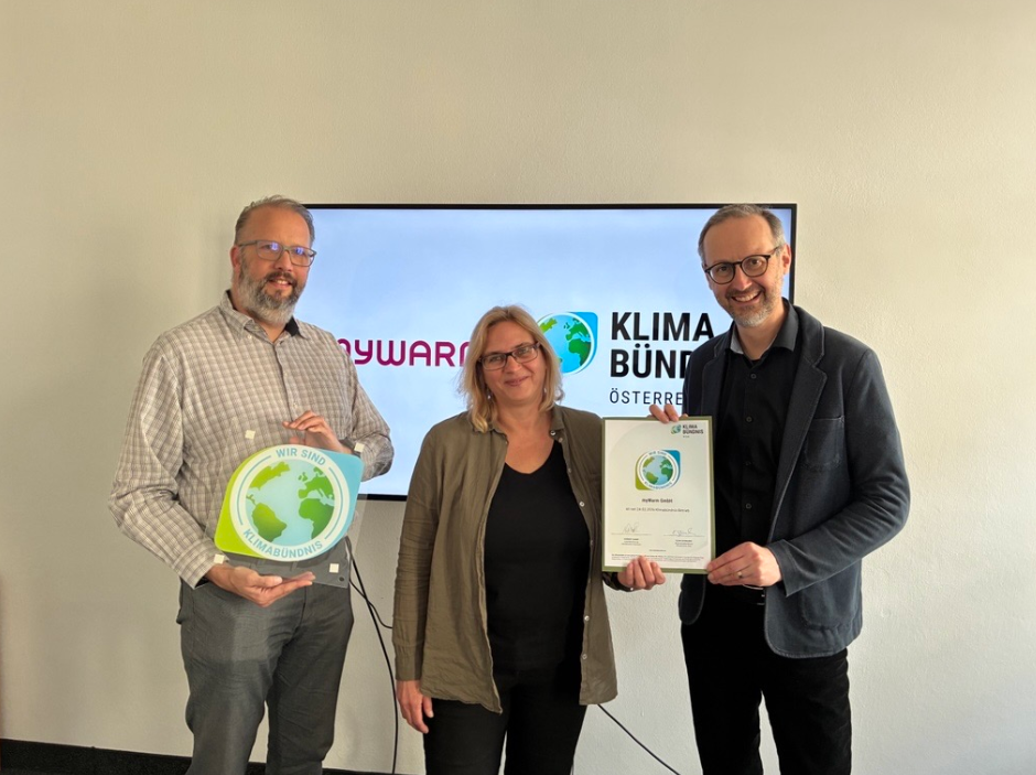 Drei menschen vor einem Bildschirm mit der Klimabündnis-Tafel in der Hand.
