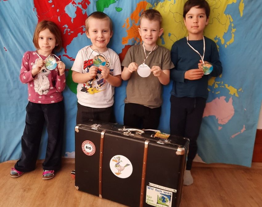 Vier Kinder stehen vor Weltkarte und hinter Klimakoffer